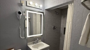 A bathroom with a toilet, sink, mirror, and shower.