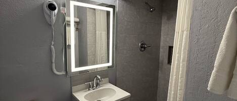 A bathroom with a toilet, sink, mirror, and shower.