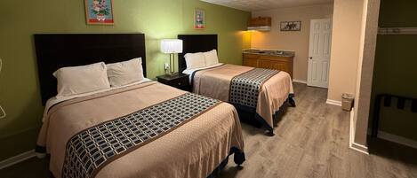 A hotel room with two beds, a small kitchenette, and a door leading to another room.