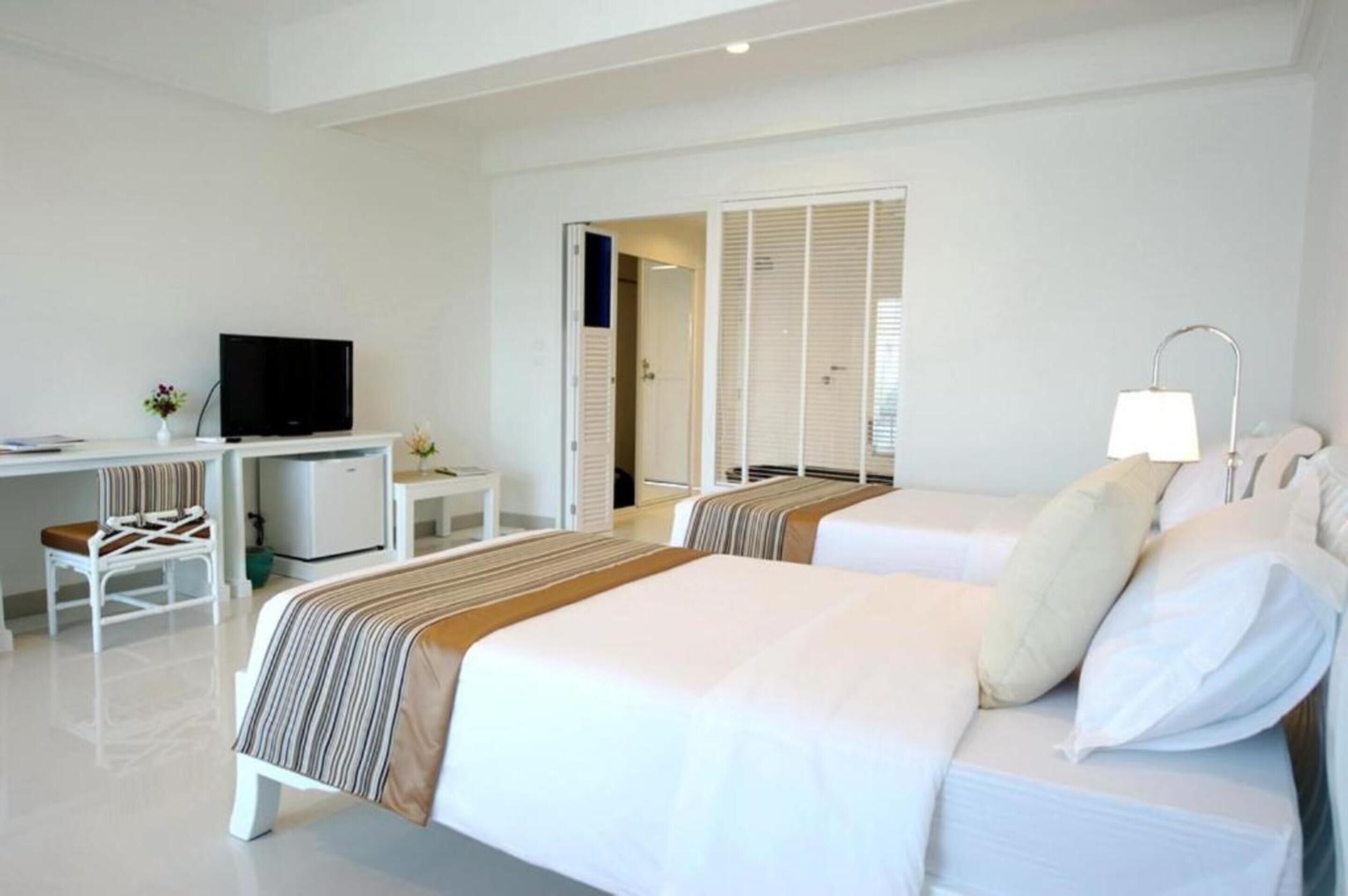 Habitación de hotel con dos camas, un escritorio con televisor, una mesita de noche y una lámpara.