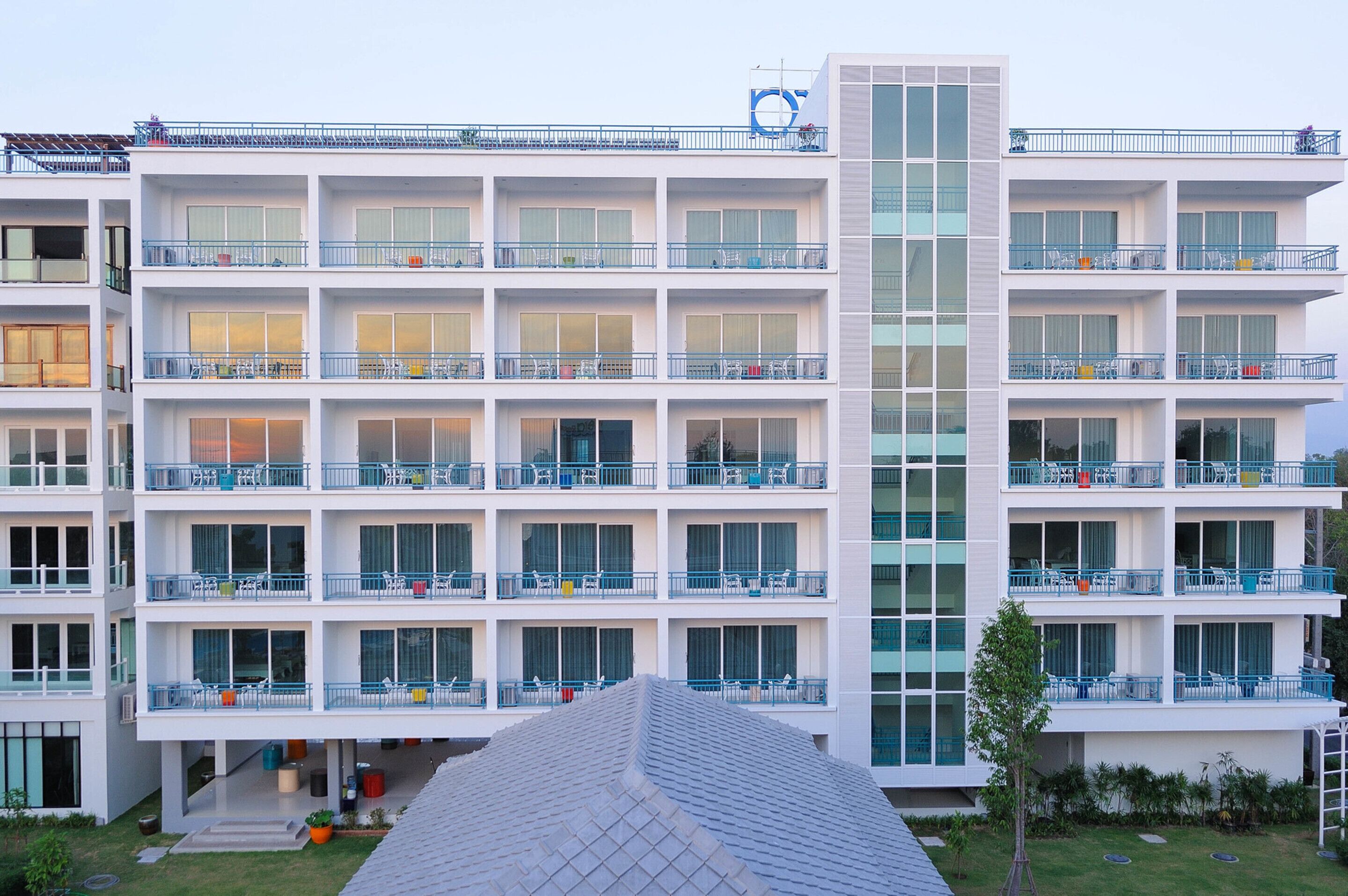 Hotel de varios pisos con balcones, amplias ventanas y un elemento vertical de vidrio en el centro.