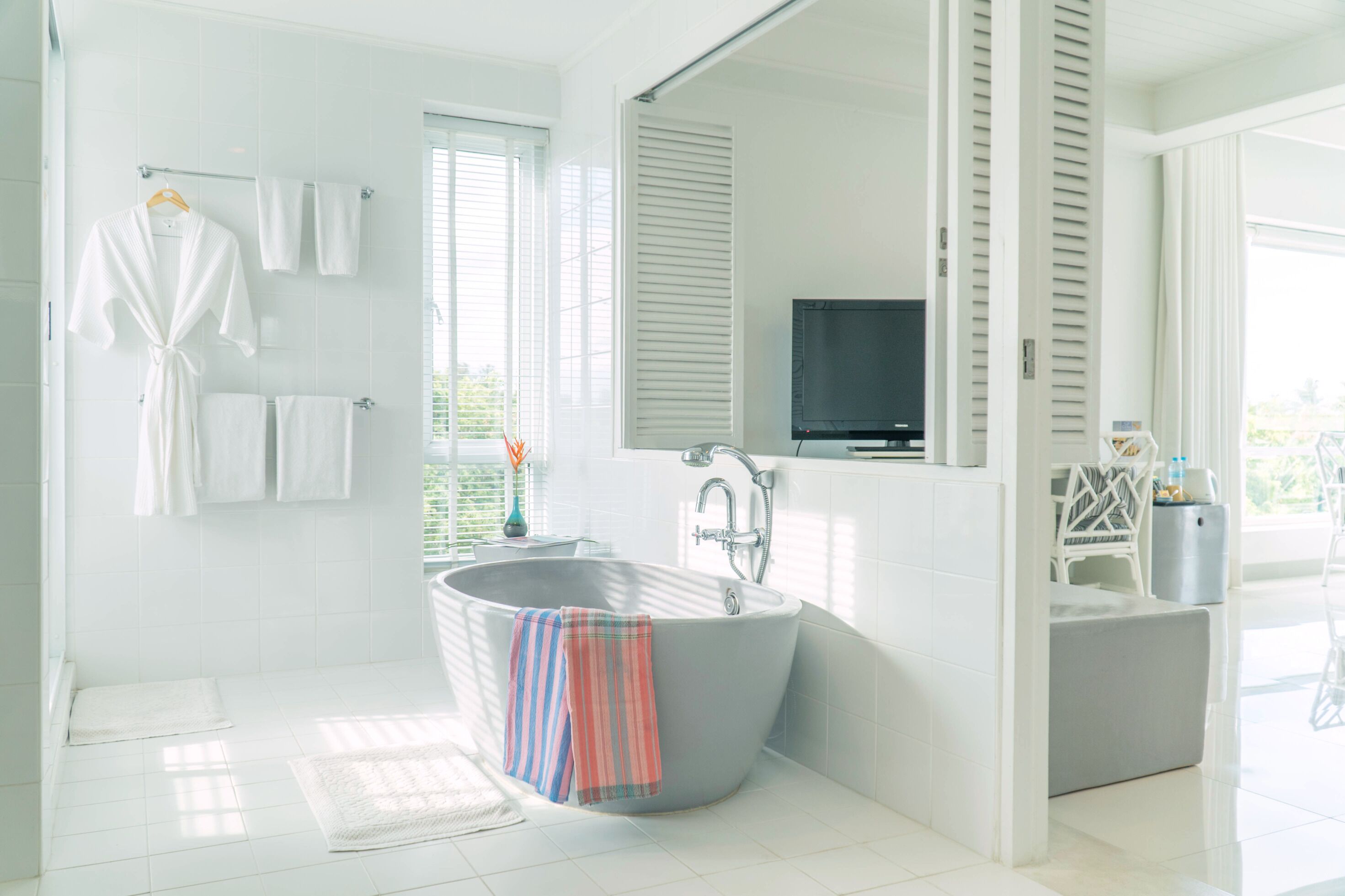 A modern bathroom with a freestanding bathtub, a large mirror, and a television.