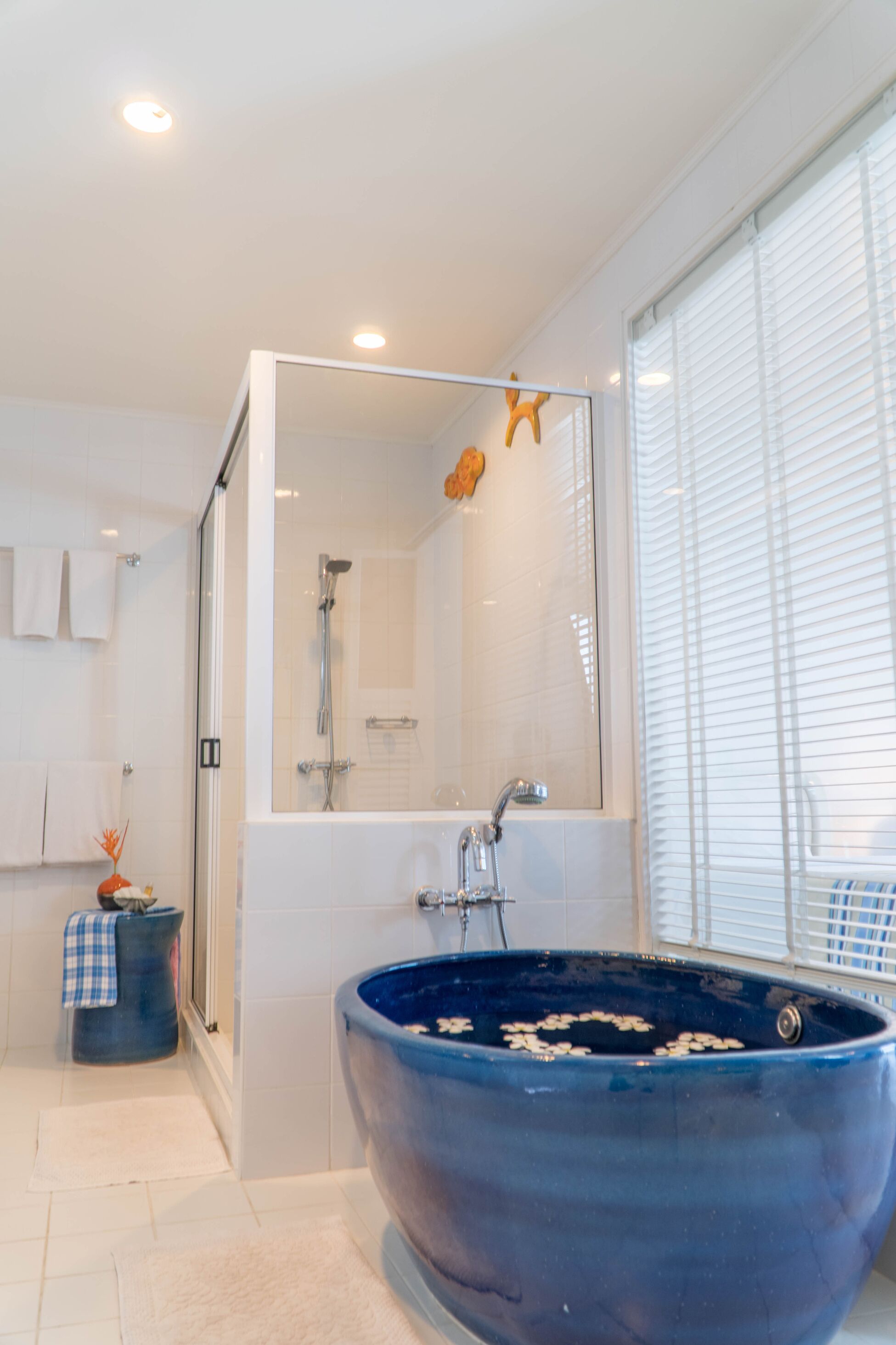 Een moderne badkamer met een groot blauw bad, een douche met glazen wanden en een raam met zonwering.
