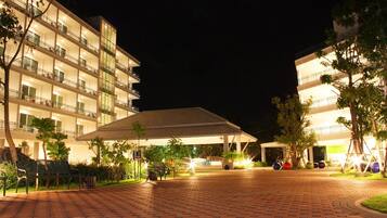 A multi-story hotel with a covered outdoor area, paved walkway, and outdoor seating.