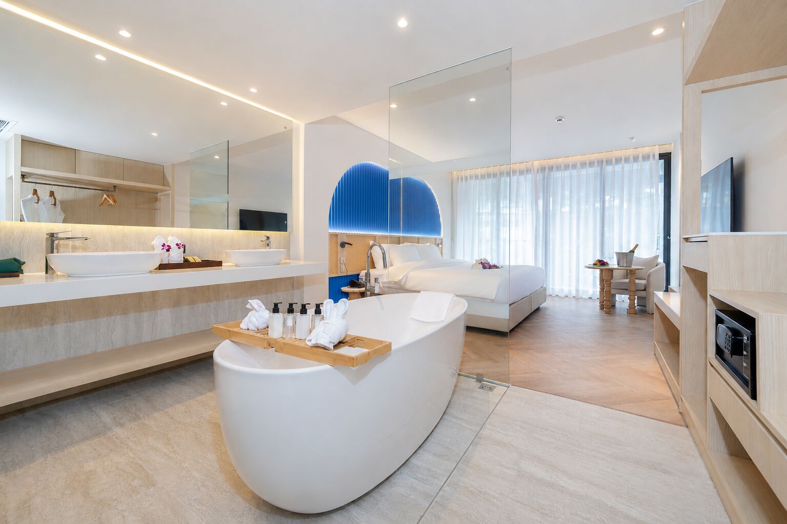 Quarto de hotel moderno com uma banheira grande, área de chuveiro separada, cama, escrivaninha e televisão.