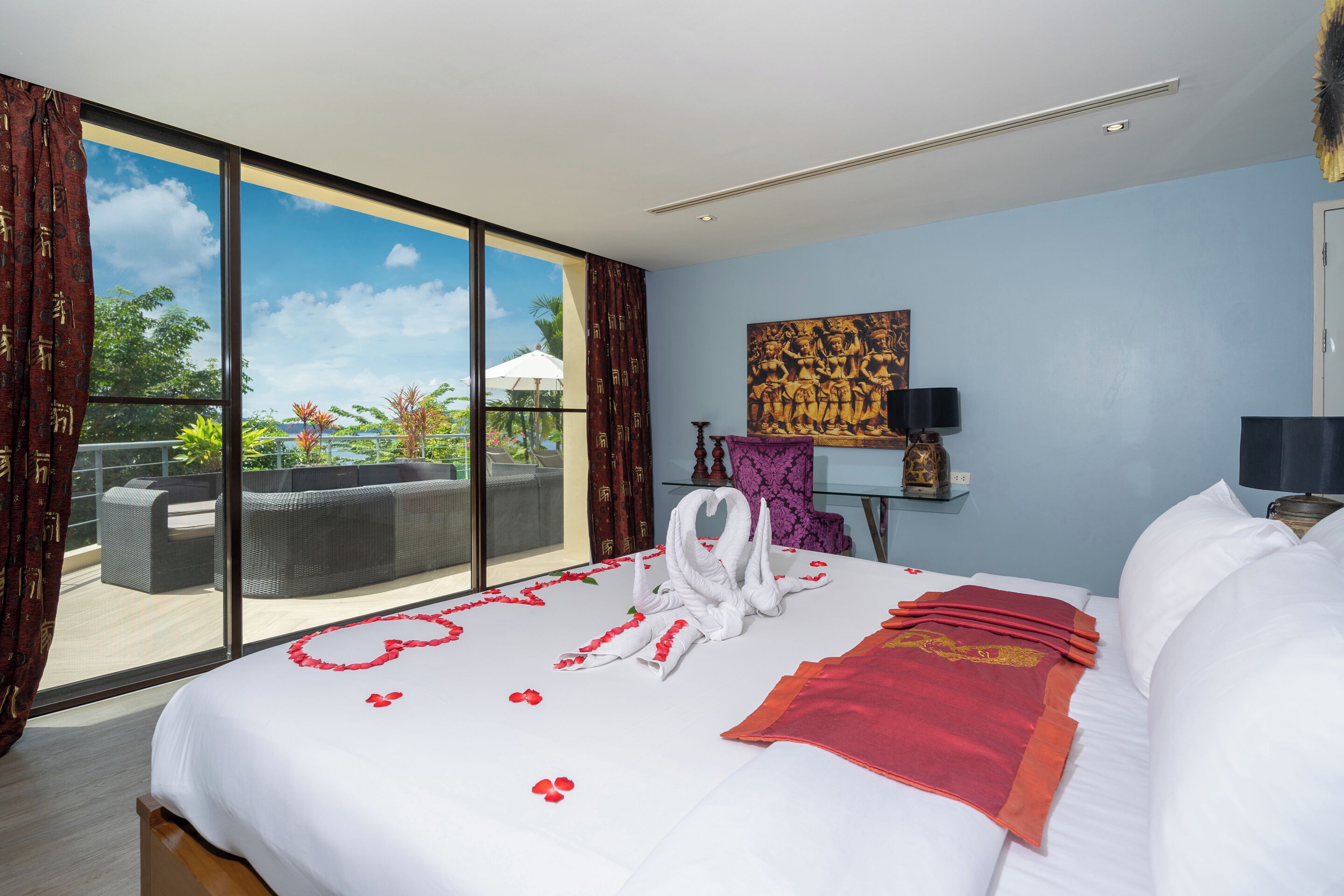 A hotel room with a large bed, a view of the outdoors, a sofa, and a painting on the wall.