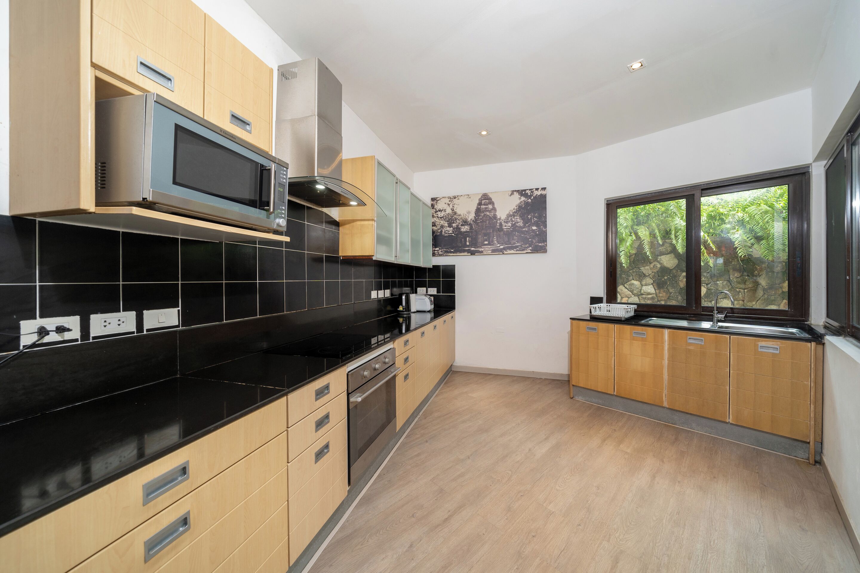 Cocina moderna con encimeras negras, armarios de madera, microondas y ventana con vista a zonas verdes.