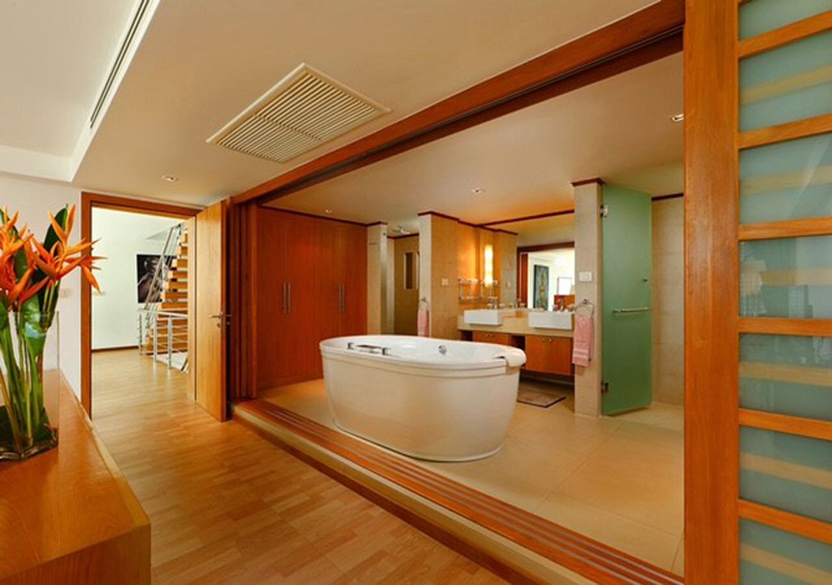 A modern bathroom with a freestanding bathtub, wooden flooring, and a visible shower area.