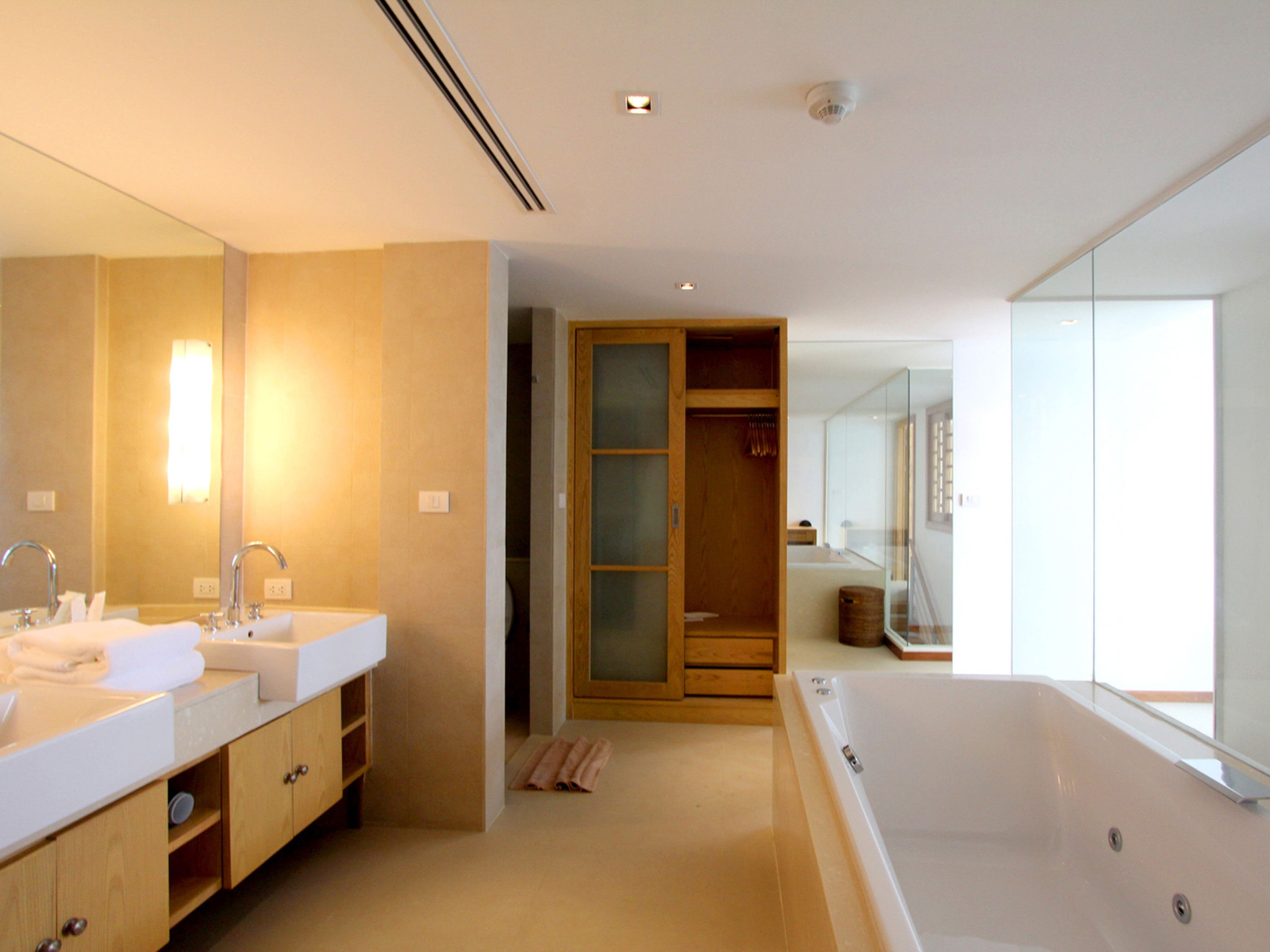 Une salle de bain moderne dotée d’un grand miroir, de deux lavabos, d’une baignoire et d’un dressing.