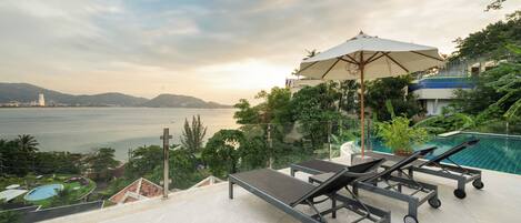 A rooftop terrace with a pool, lounge chairs, and a large umbrella.