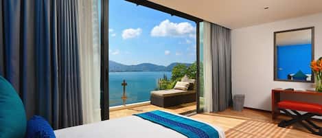 A hotel room with a large bed, a sofa by the window, and a view of the sea.