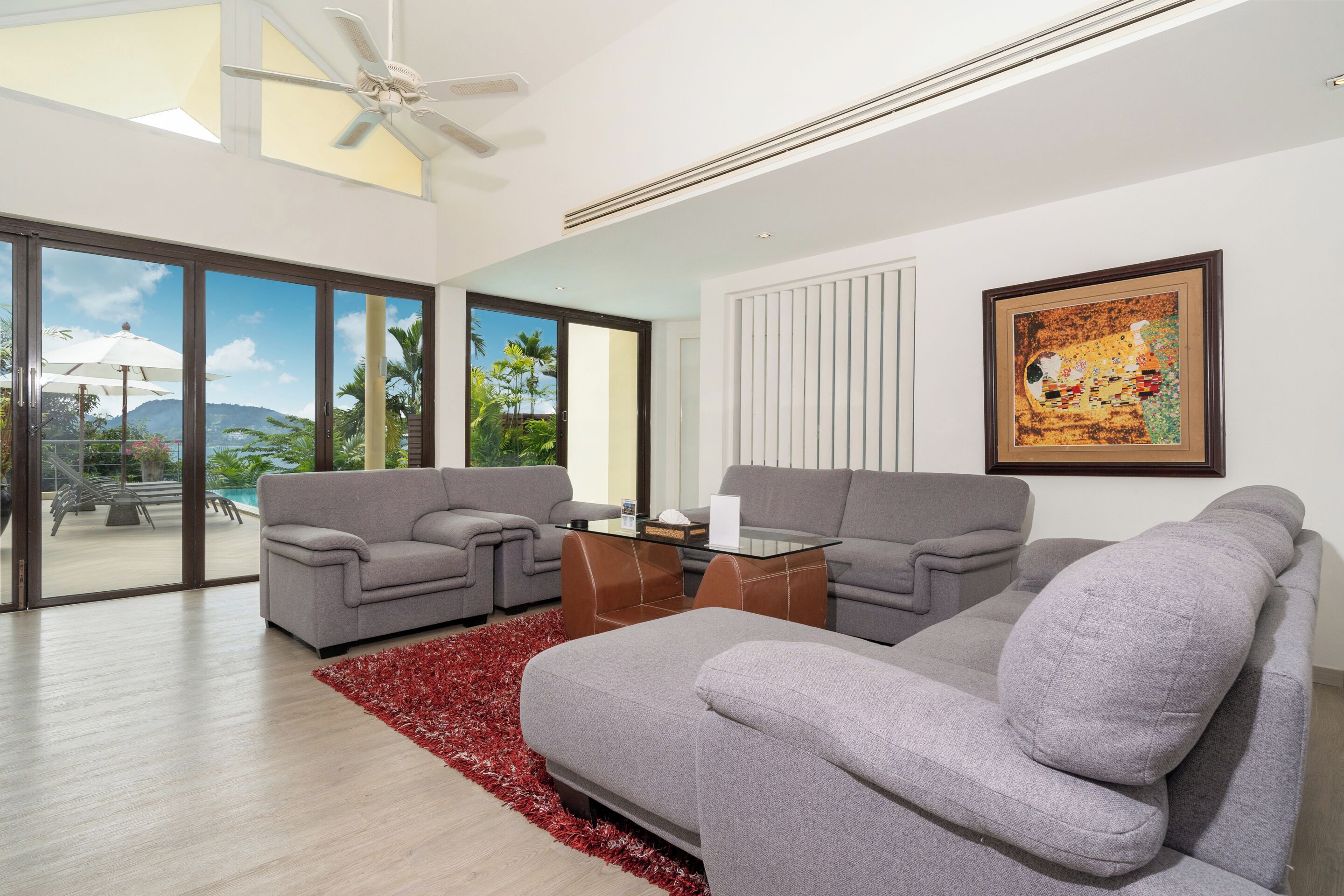 A modern living room with two grey sofas, a glass coffee table, and a red rug.