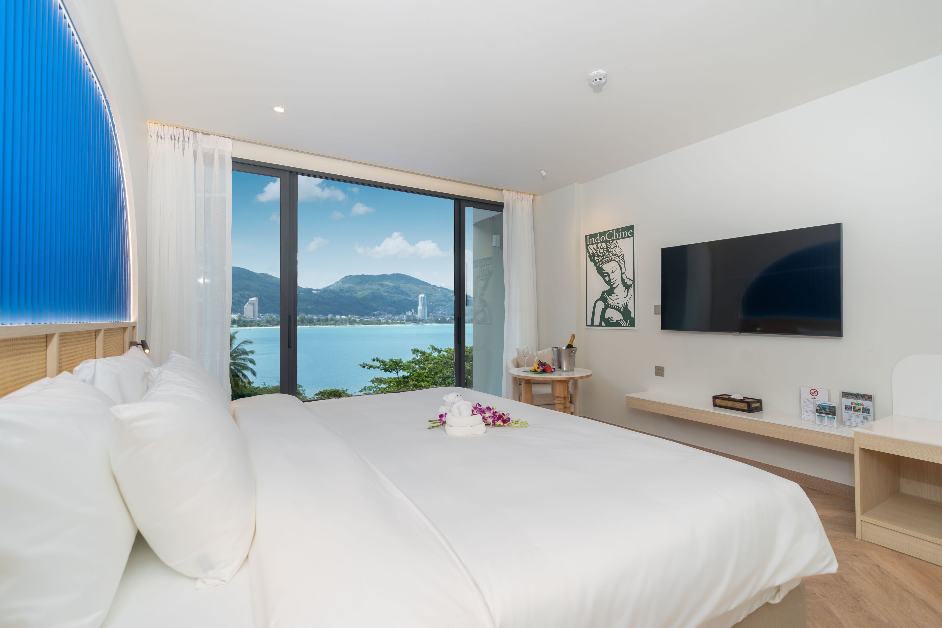 Habitación de hotel con una cama grande, televisor, una mesita y vista a un cuerpo de agua.