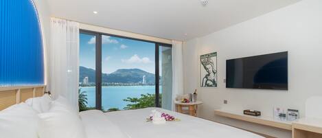 Habitación de hotel con una cama grande, televisor, una mesita y vista a un cuerpo de agua.