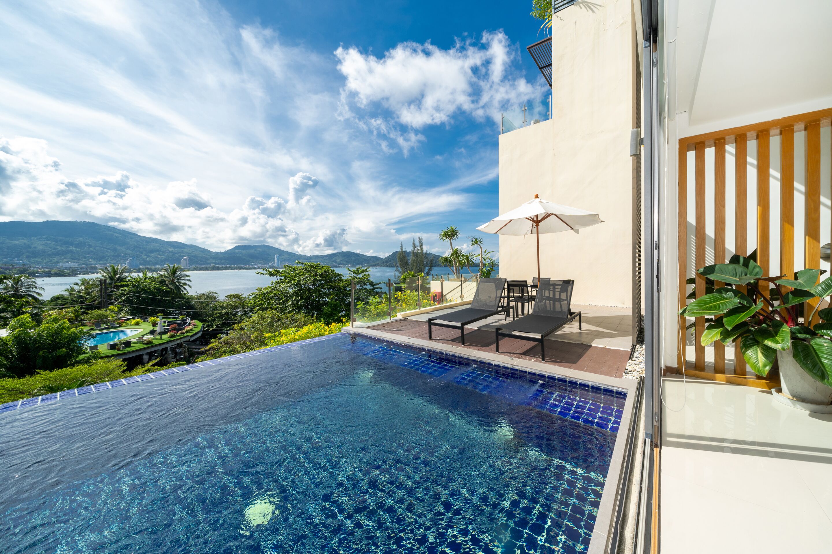 Ein Infinity-Pool mit freiem Blick auf die Berge und eine Poollandschaft mit Liegestühlen und Sonnenschirm.