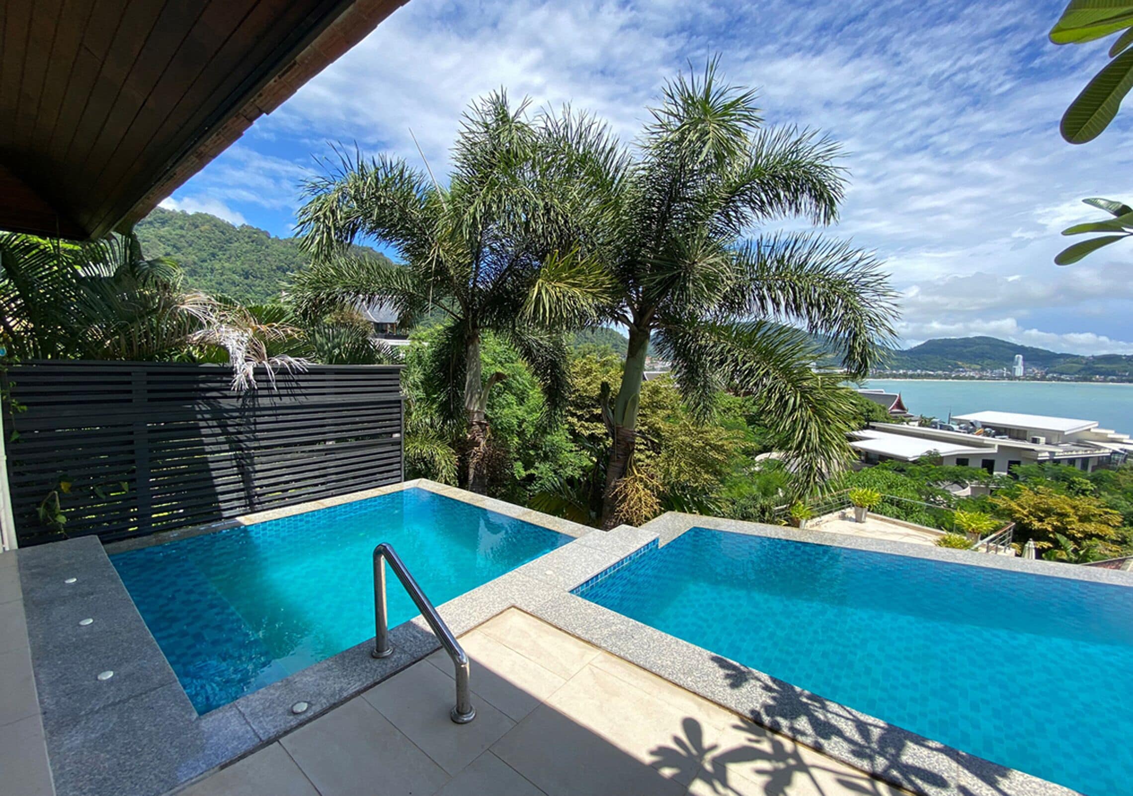 A pool area with two separate pools, surrounded by lush greenery and a view of the sea.