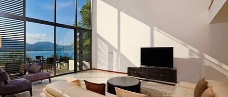 Una sala de estar moderna con un sofá grande, un televisor y vistas al exterior a través de ventanas de techo a suelo.