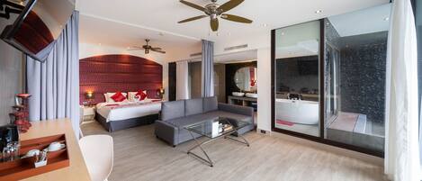 A modern hotel room with a large bed, a sofa, a glass coffee table, and a ceiling fan.