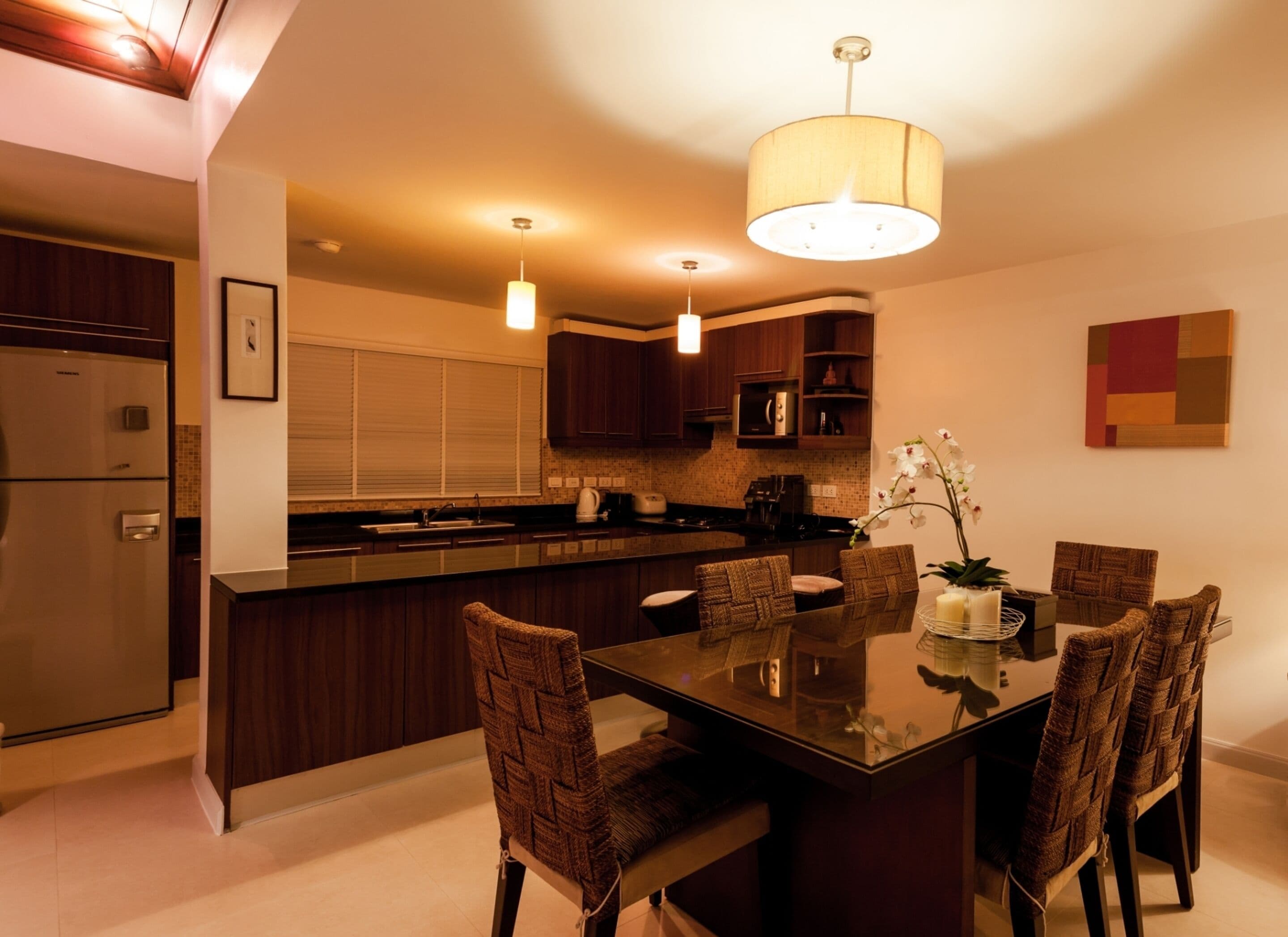 A modern kitchen with dark wood cabinets, a central island with seating, pendant lighting, and a dining table with chairs.