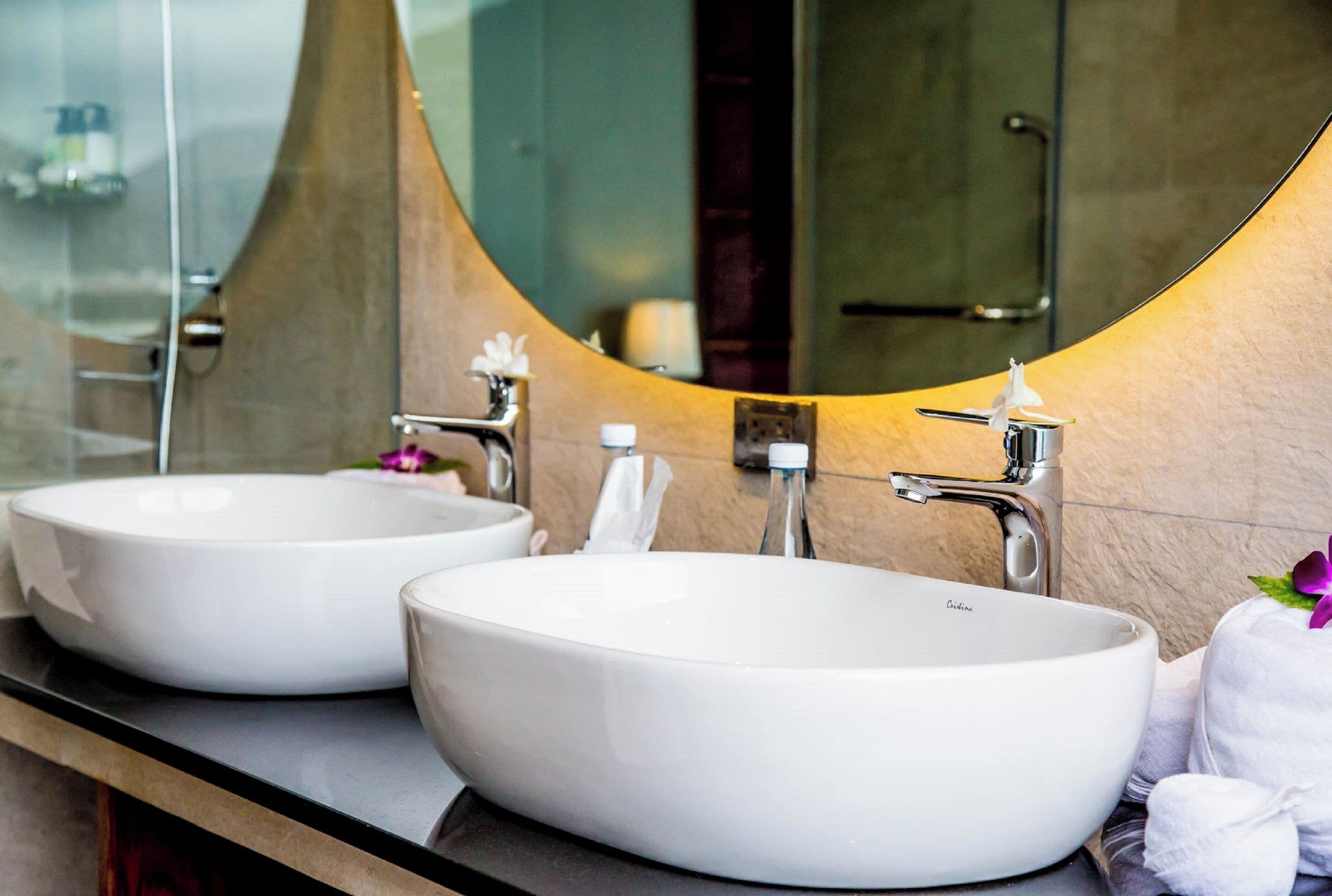 Two white ceramic sinks with modern faucets, a mirror with a curved frame, and a towel rack with a white towel.