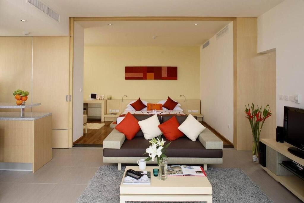 Una habitación de hotel moderna con sofá cama, una mesa de centro, televisor y un pequeño rincón de cocina.