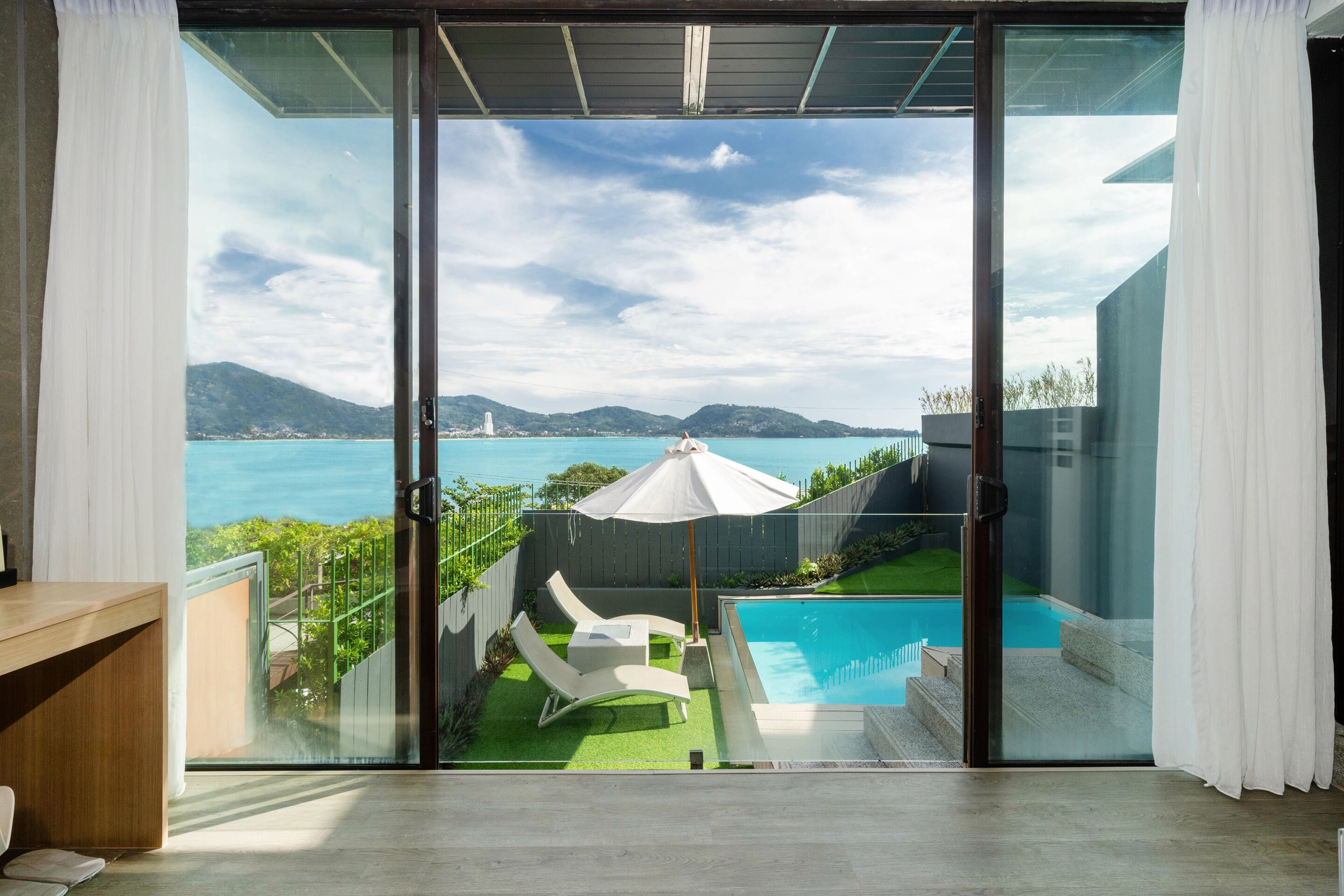 A modern room with a sliding glass door leading to a balcony with a pool and outdoor furniture.