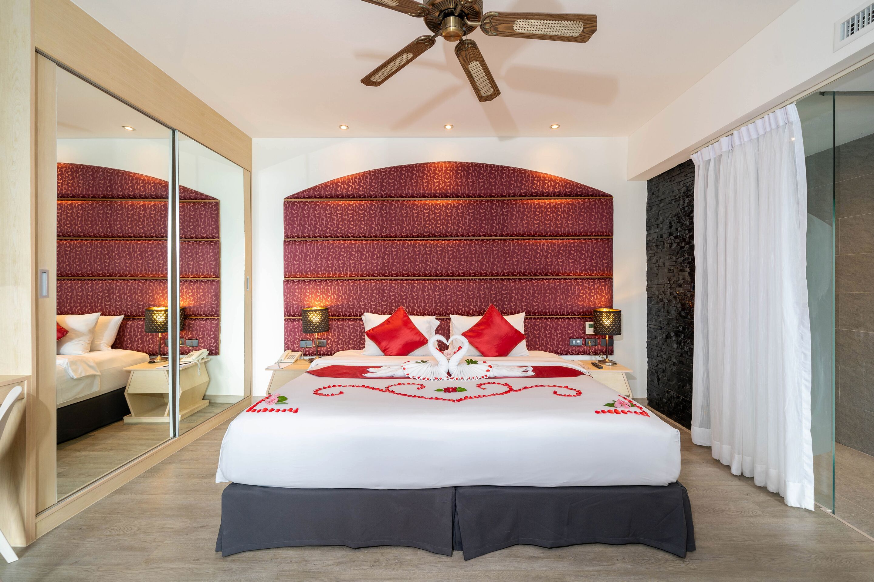 A hotel room with a large bed, a glass shower enclosure, and a red patterned headboard.