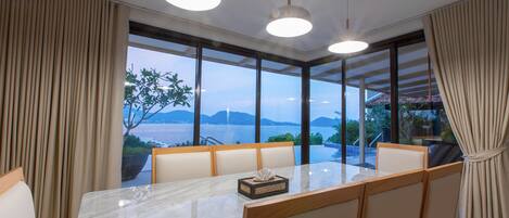 A dining area with a large table, chairs, and a view of the sea.