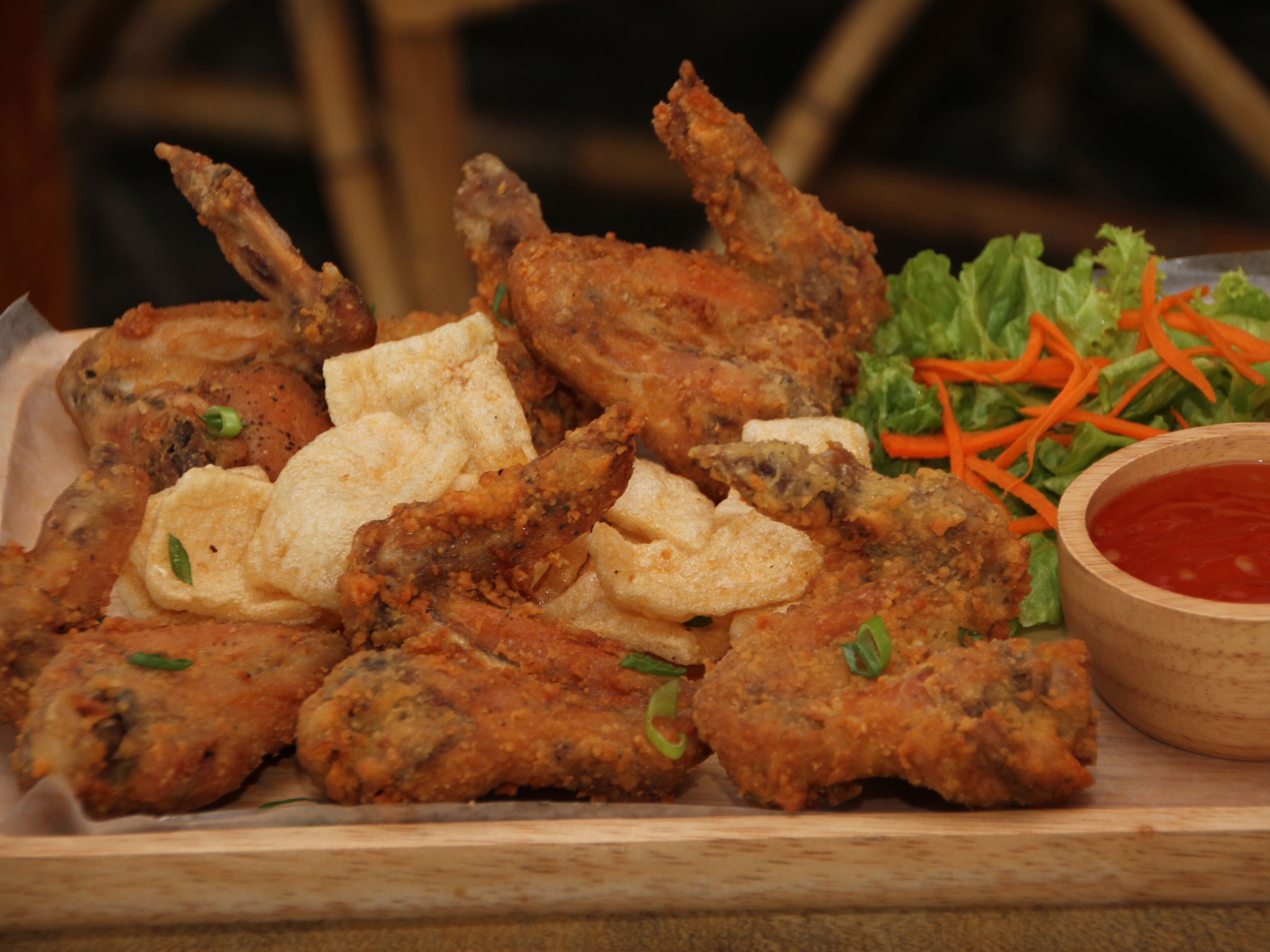 A tray of fried chicken wings with a side of shredded carrots and a small bowl of sauce.