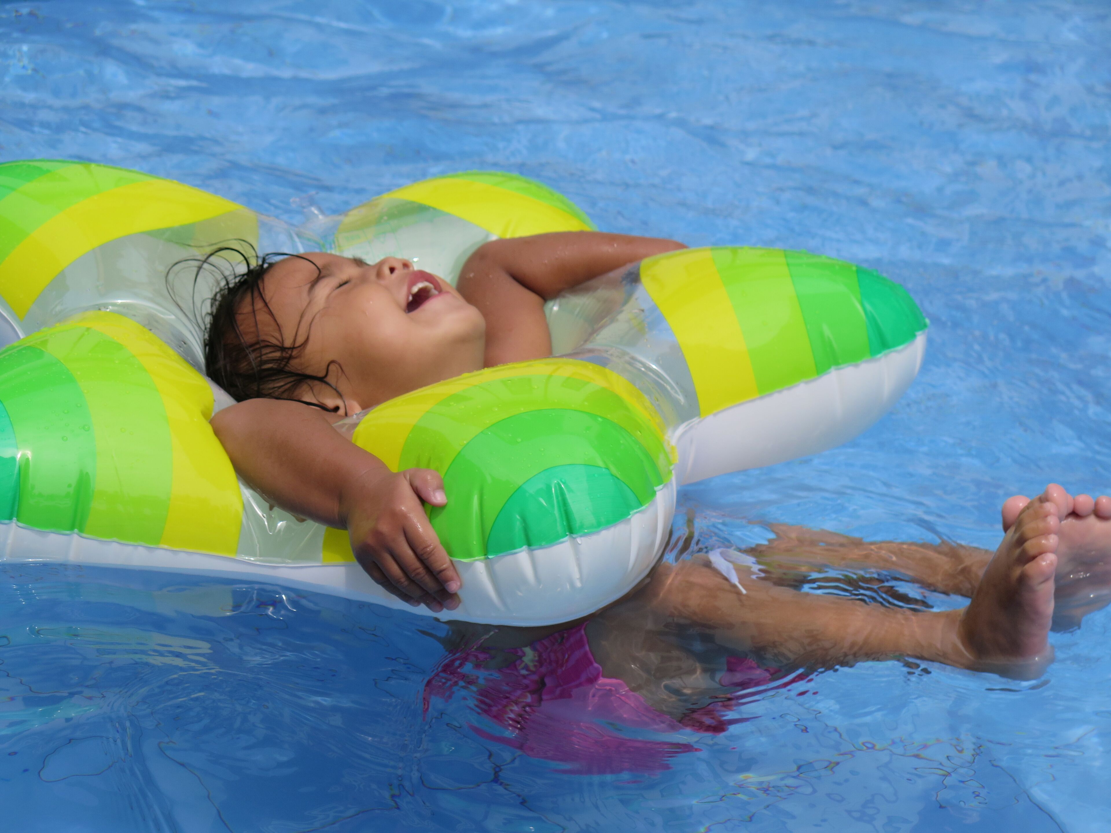 A child in a pool using a green and white inflatable float.