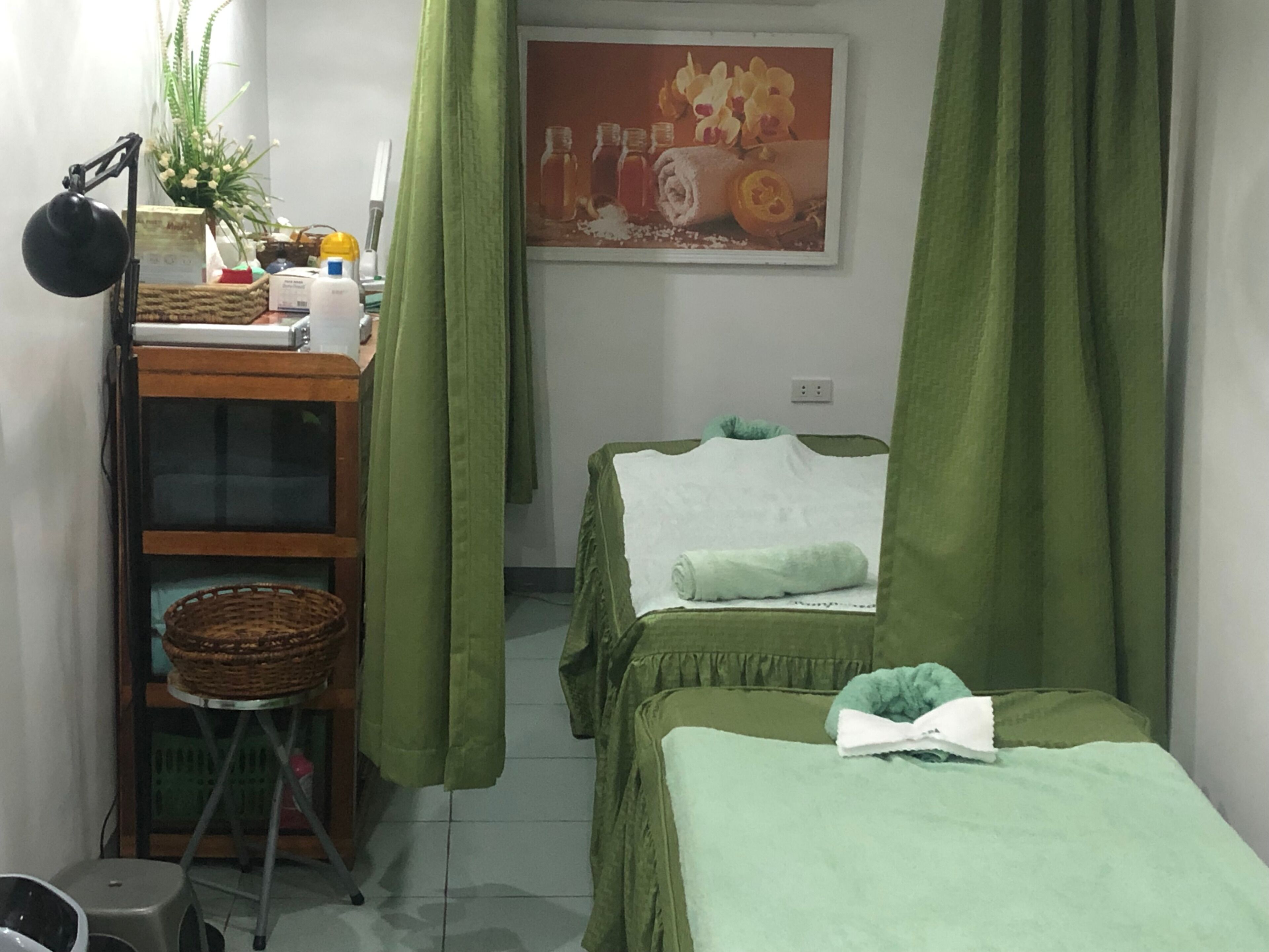 A small, neatly arranged room with two beds, a desk, a chair, a plant, and a poster on the wall.