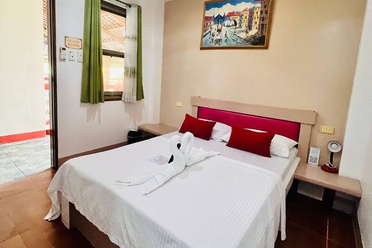 Une chambre d’hôtel avec un grand lit, des oreillers rouges, une tête de lit, une table de chevet avec une lampe et un tableau au mur.