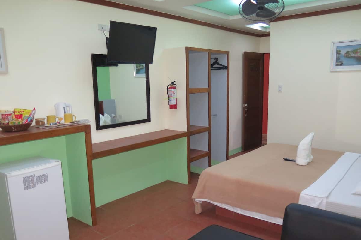 Une chambre d’hôtel équipée d’un lit, d’un bureau avec un ordinateur, d’un petit réfrigérateur, d’un miroir, d’une armoire et d’un extincteur.