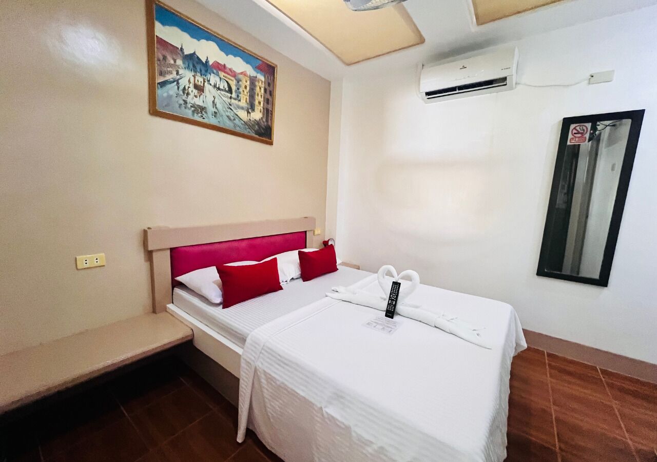 Habitación individual con cama, cabecera, un cuadro en la pared, equipo de aire acondicionado y ventana con letrero de prohibido fumar.