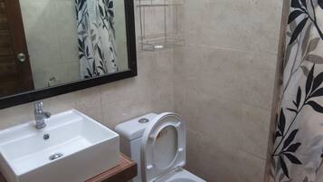 Une salle de bain avec un lavabo blanc, des toilettes et un rideau de douche orné d’un motif de feuilles.