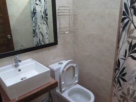 Une salle de bain avec un lavabo blanc, des toilettes et un rideau de douche orné d’un motif de feuilles.