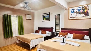 Ein Hotelzimmer mit zwei Betten, Holzboden, Deckenventilator, einem Bild an der Wand und einem Fenster mit grünen Vorhängen.