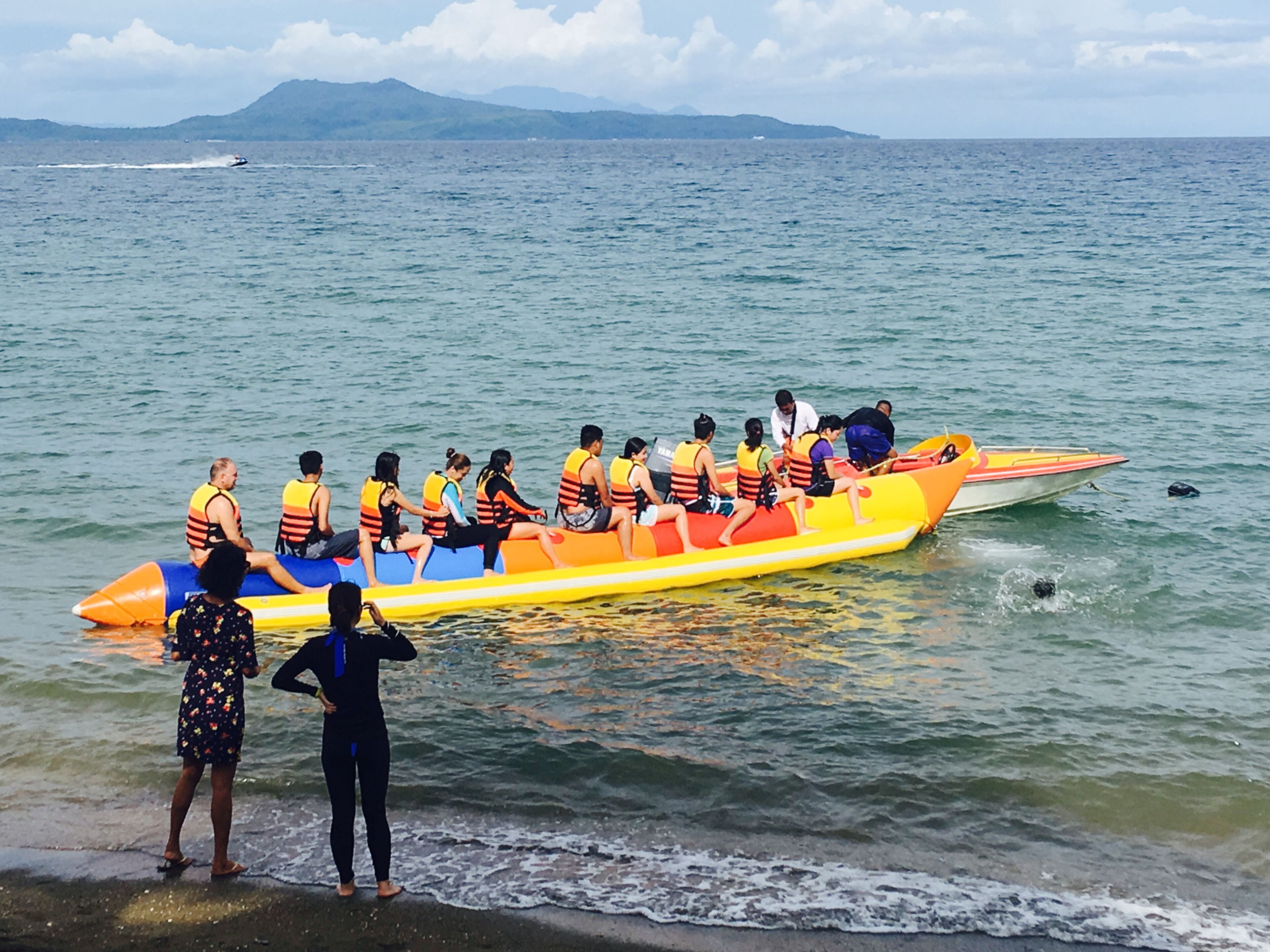 Un groupe de personnes se trouve dans un radeau coloré sur une étendue d’eau, avec des montagnes en arrière-plan.