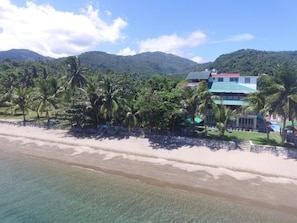 A beachfront property with a large house, palm trees, and mountains in the background. - BADLADZ Beach and Dive Resort (Puerto Galera)