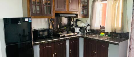 Una cocina con armarios de madera oscura, un refrigerador negro, una estufa y un microondas.