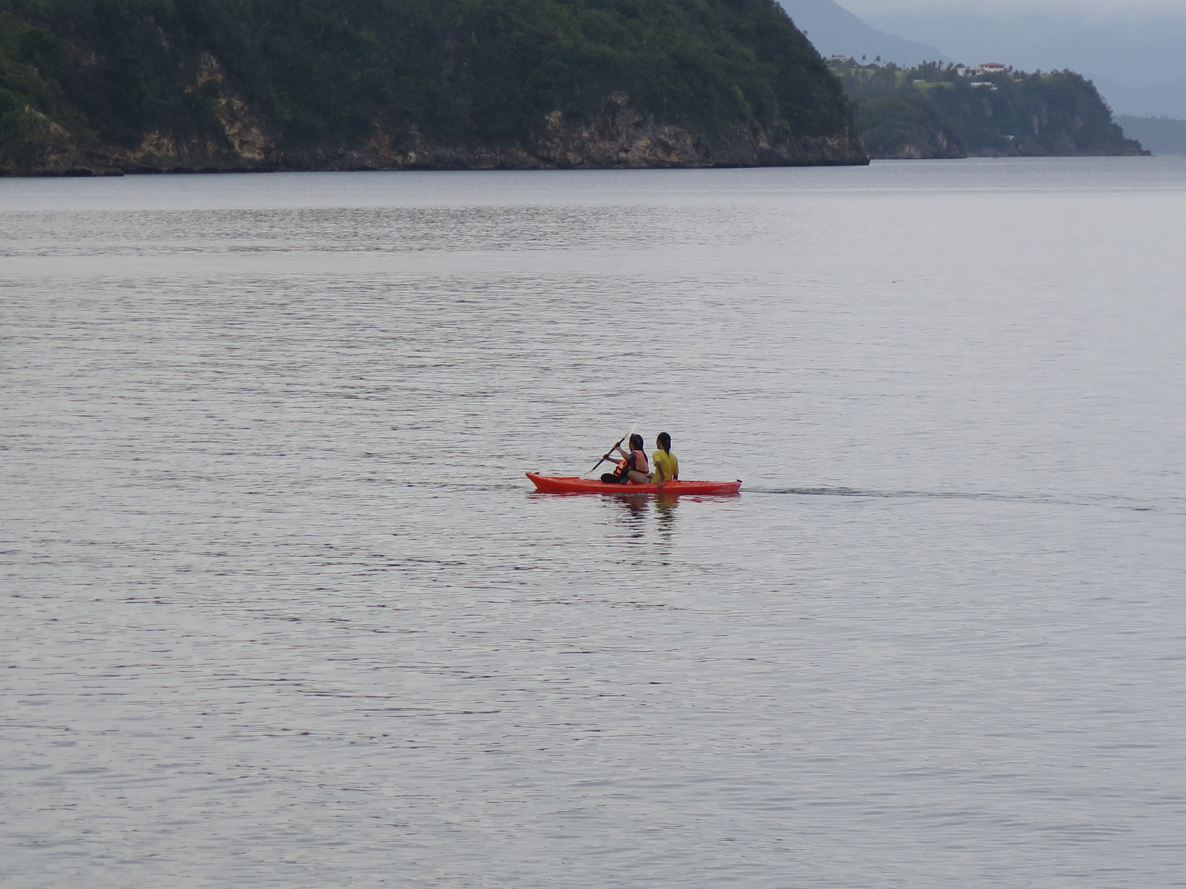 A calm body of water with a red kayak carrying two people.