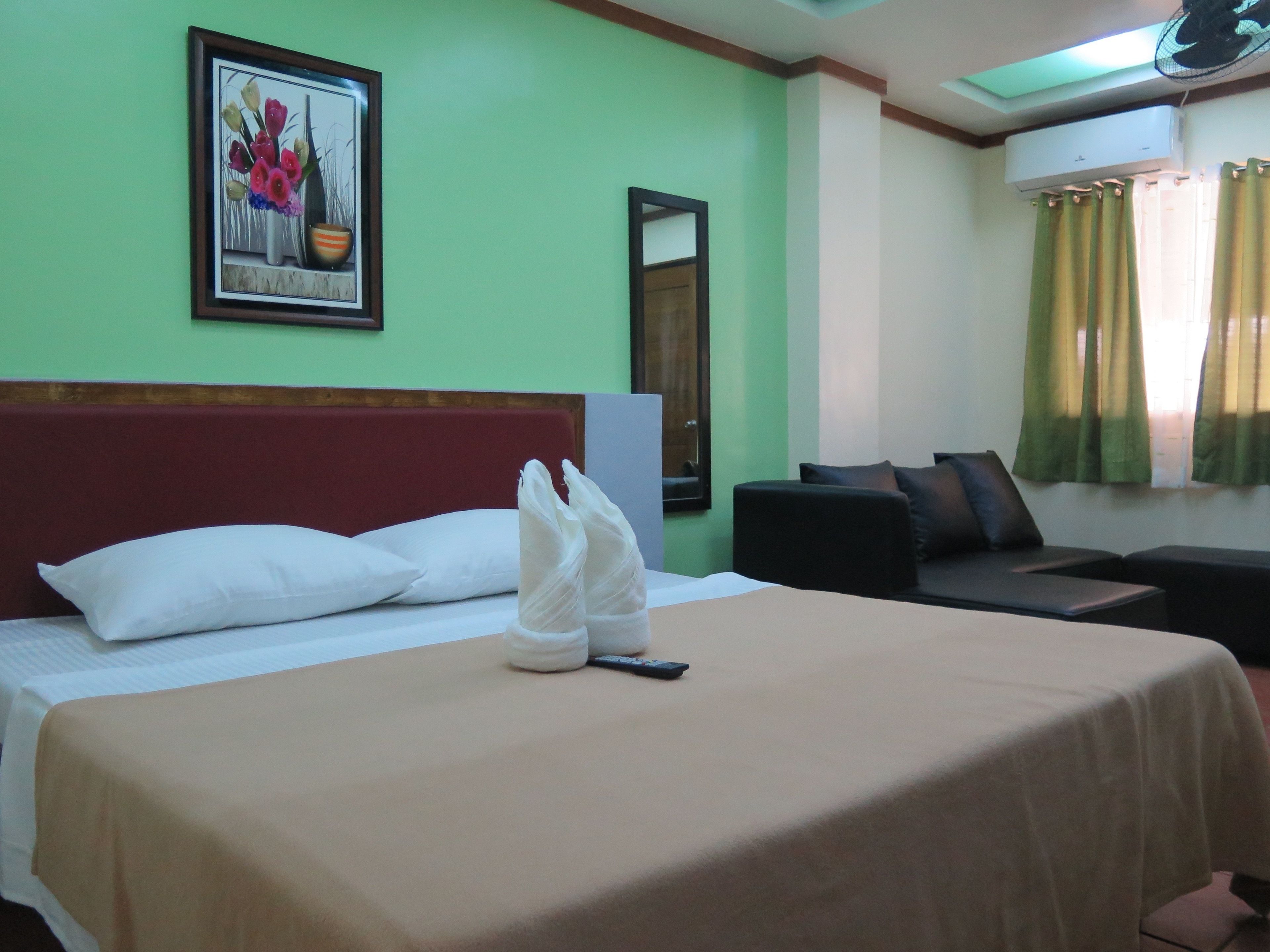 A hotel room with a bed, a desk, a chair, a window with curtains, and a wall-mounted air conditioner.