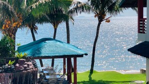 Ein Poolbereich mit einer Reetdach-Sonnenschirm, weißen Korbmöbeln und Blick auf das Meer.