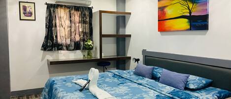 A bedroom with a bed, a bedside table, an air conditioning unit, a window with curtains, a painting on the wall, and a fan.