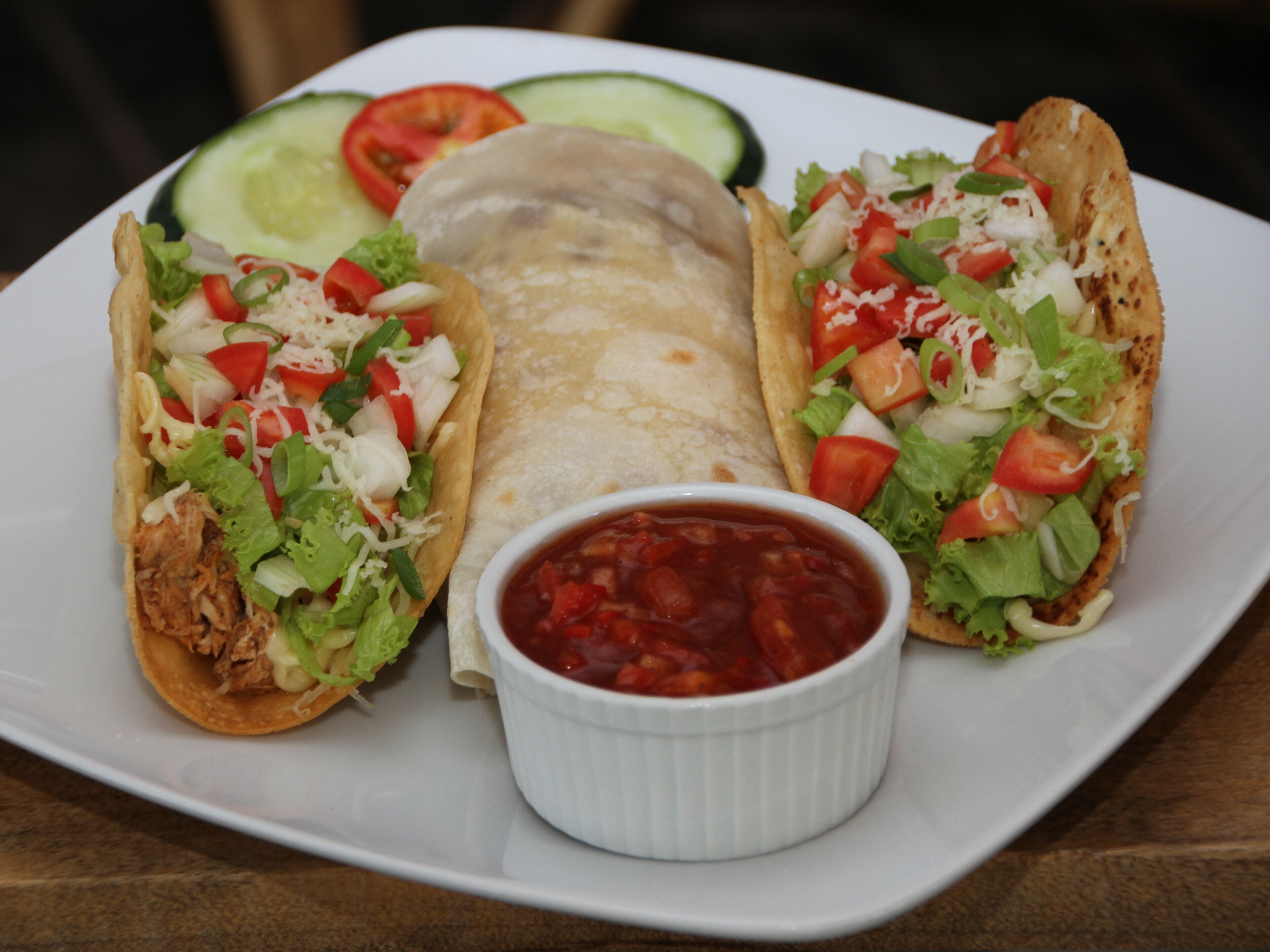 Tre tacos accompagnati da una porzione di salsa su un piatto bianco.
