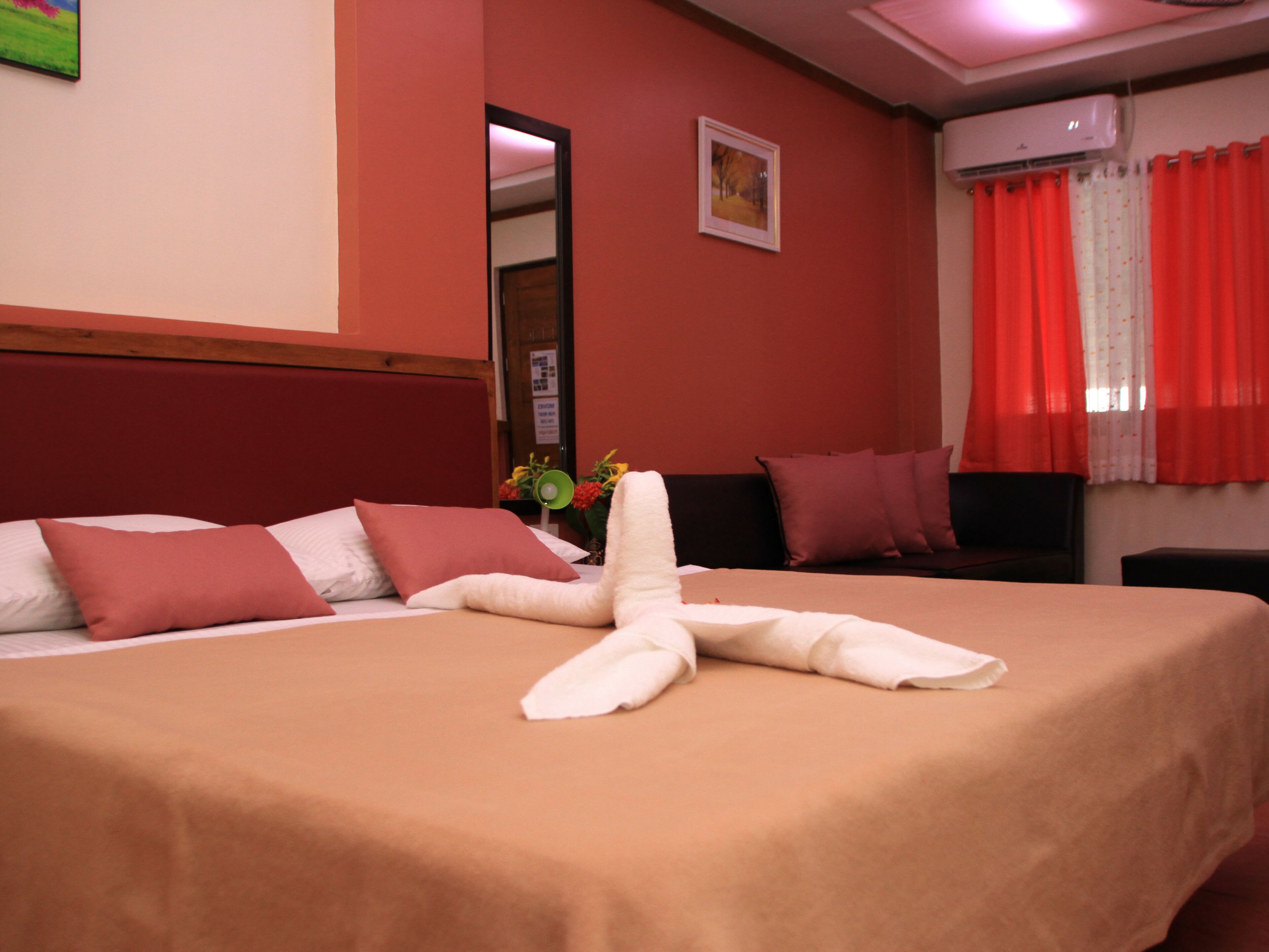 A neatly made bed with a white towel in the center, a wooden headboard, and a red wall with a framed picture.
