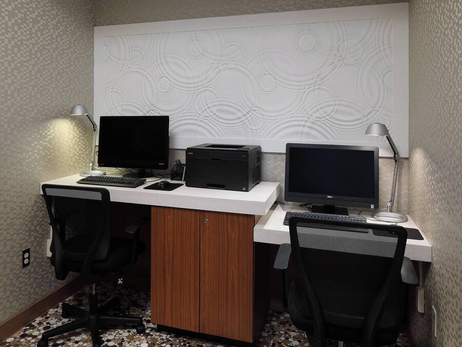 A business library workspace with two desks, computers, chairs, and a patterned wall.