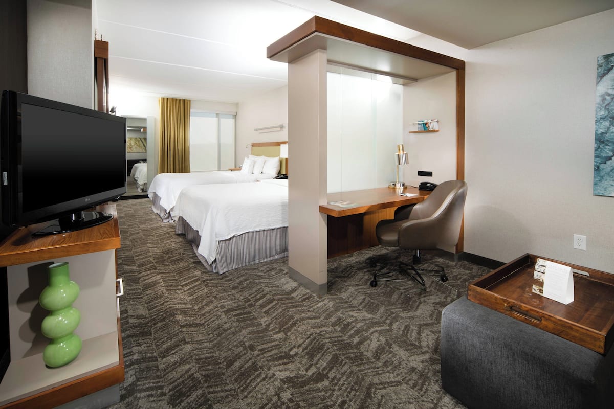 A hotel room with a TV, two beds, a desk, a chair, and a small table.