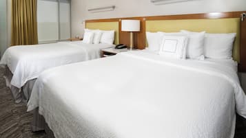 Una camera d'albergo con due letti, un comodino con una lampada e una finestra con tende.