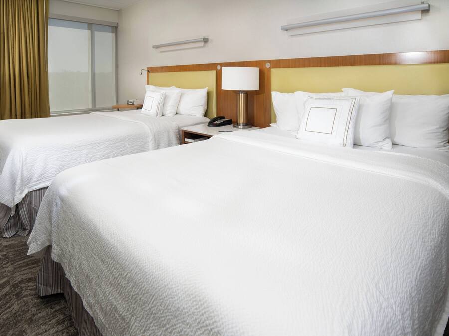 Habitación de hotel con dos camas, una mesita de noche con lámpara y una ventana con cortinas.